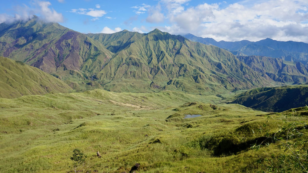 Mountains covered in green meadows rising up to touch the clouds.